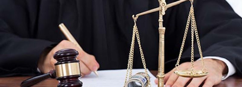 Midsection of male judge signing document with mallet and scale on desk